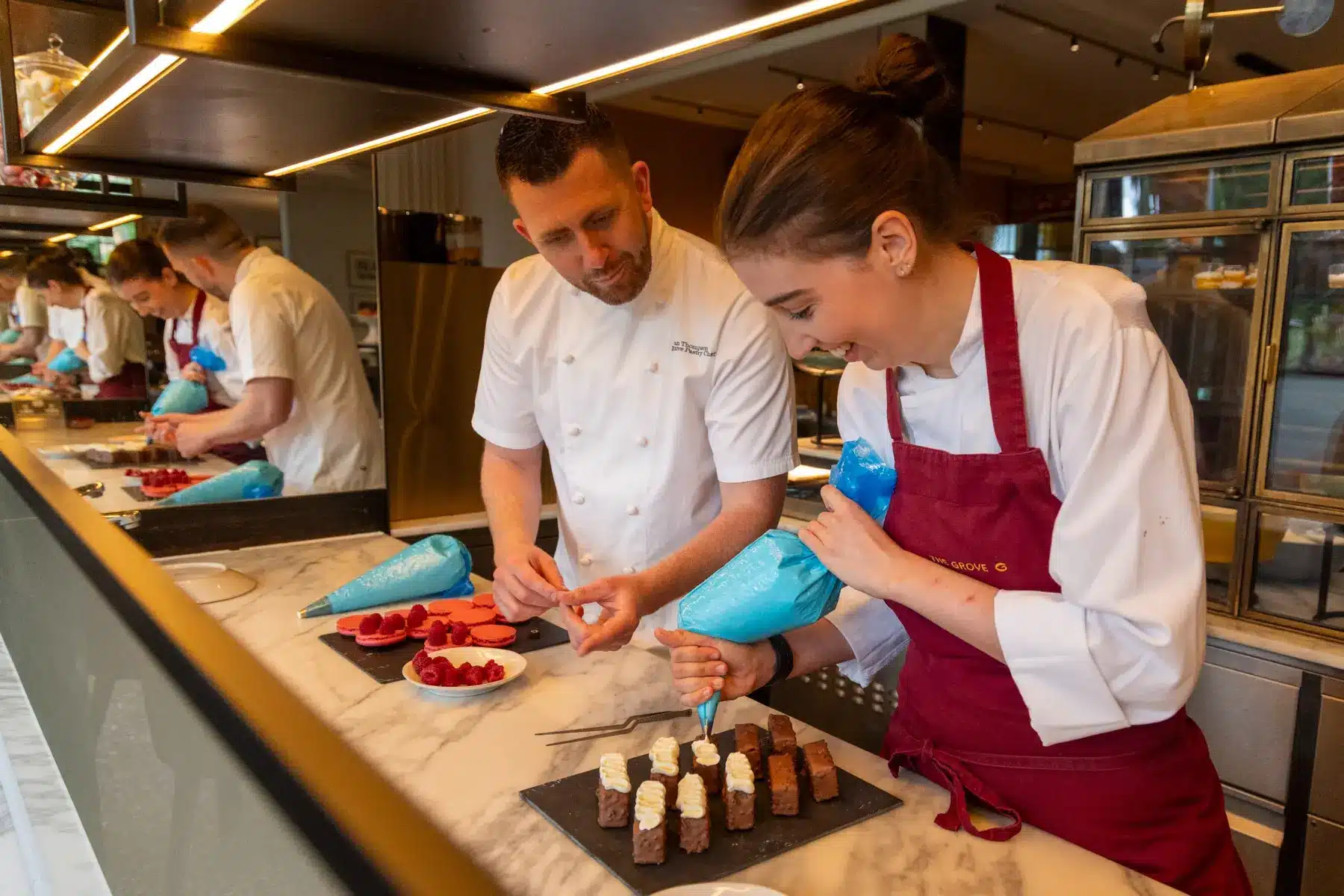 A chef supporting a young pastry chef as she pipes desserts in a professional kitchen